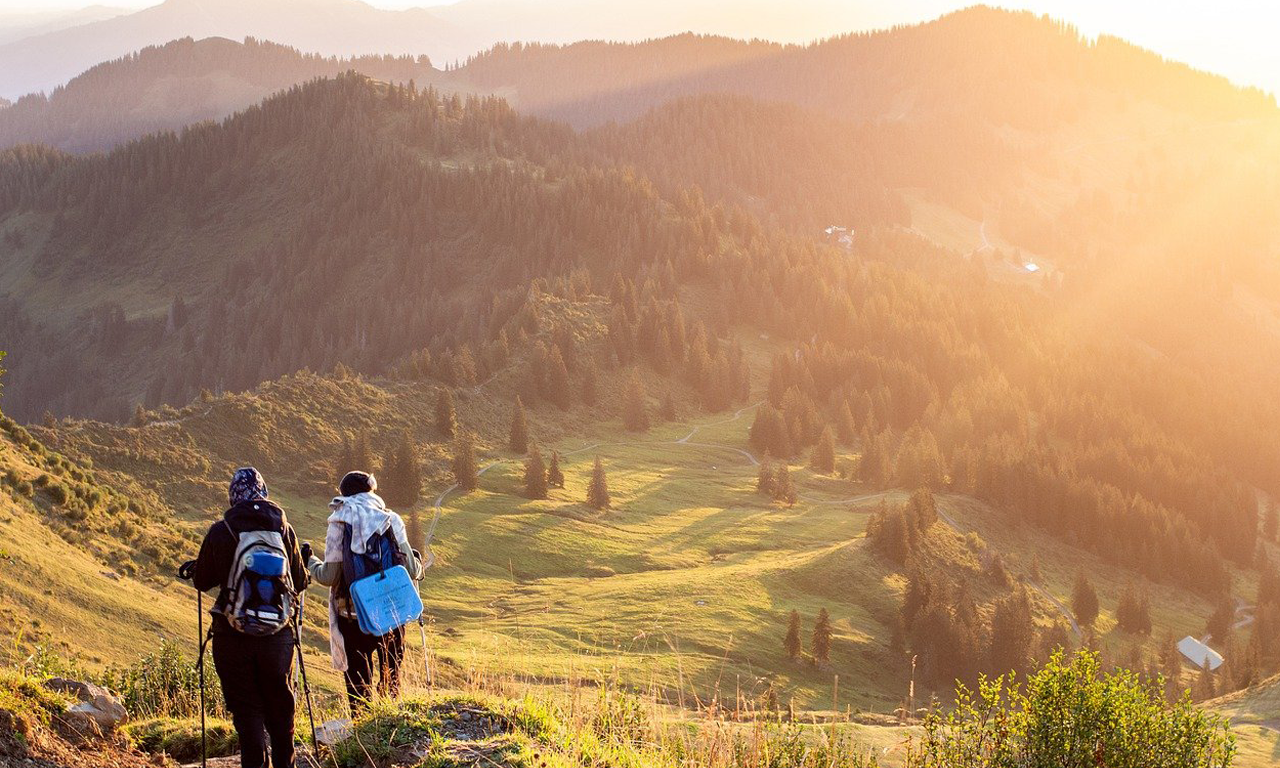 Gehle Reisen - zwei Personen wandern in den Bergen, der untergehenden Sonne entgegen